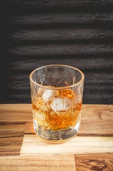 A beautiful glass of wiskey on the Rocks, on a black background, and a wooden table.