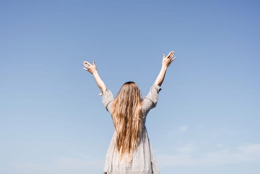 A woman with long hair is standing on the beach, looking up at the sky. She is wearing a dress and she is happy