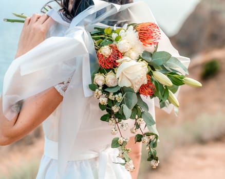 A woman is holding a bouquet of flowers, with a white dress and a bow. The flowers are a mix of red and white