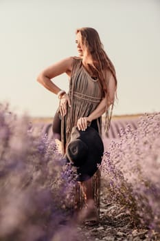 A woman is standing in a field of purple flowers, wearing a black dress and a black hat