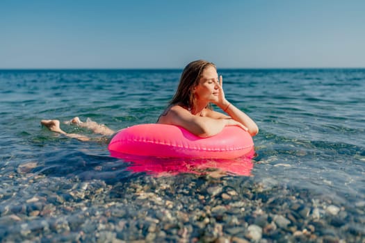 A woman is laying in a pink inflatable tube in the ocean. The water is calm and the sky is clear. The woman is relaxed and enjoying her time in the water