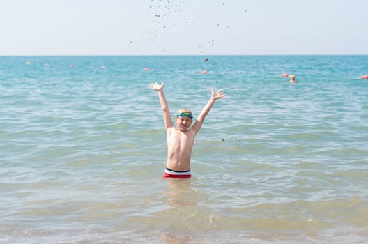 Child playing happily in the sea with hands up, Bright sunlight illuminates the scene, Concept of children's fun and happiness on the beach in Turkey