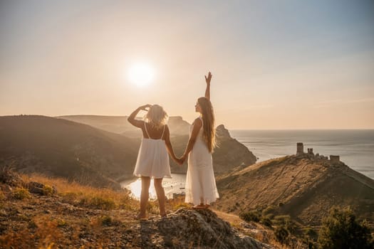 Two women are standing on a hill overlooking the ocean. They are holding hands and looking out at the water. The scene is peaceful and serene, with the sun shining brightly in the background