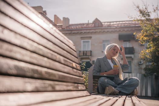 A woman sitting on a bench with a cell phone in her hand. She is wearing a suit and she is working on her phone