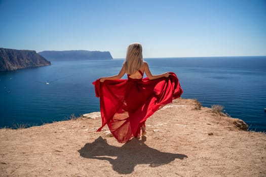 A woman in a red dress stands on a cliff overlooking the ocean. The scene is serene and peaceful, with the woman's dress adding a touch of elegance to the landscape