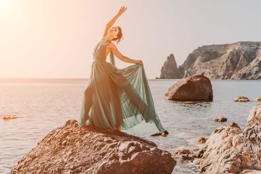 Woman green dress sea. Woman in a long mint dress posing on a beach with rocks on sunny day. Girl on the nature on blue sky background