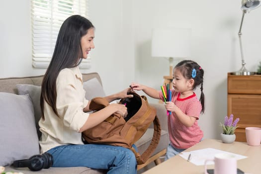Asian mother and daughter enjoy a playful moment while preparing school supplies, emphasizing a supportive school routine.