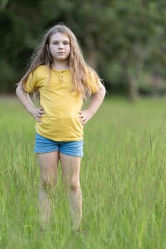 Young girl is standing in a tall grass field with her hands on her hips