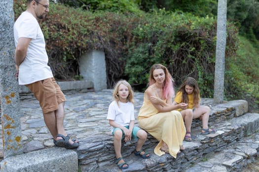 Family is spending time together in the park, sitting on stone steps surrounded by greenery