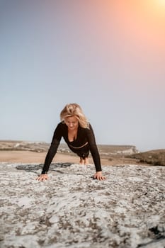 A woman in black athletic wear does push ups on a rocky cliff with a scenic view behind her.