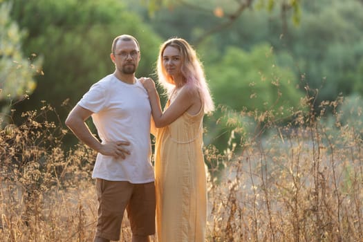 Man and a woman are posing in a field at golden hour