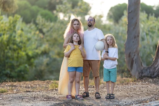 Family of four is posing together in a park while holding a volleyball