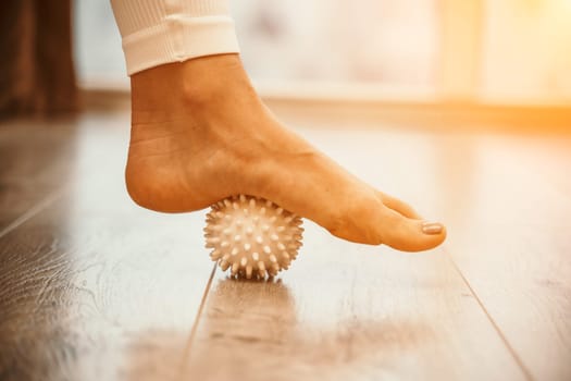 Athletic slim caucasian woman doing thigh self-massage with a massage ball indoors. Self-isolating massage.