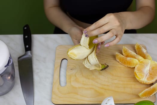 Girl peels banana on kitchen counter while making sports drink in a blender. Preparing ingredients to blend and create healthy drink