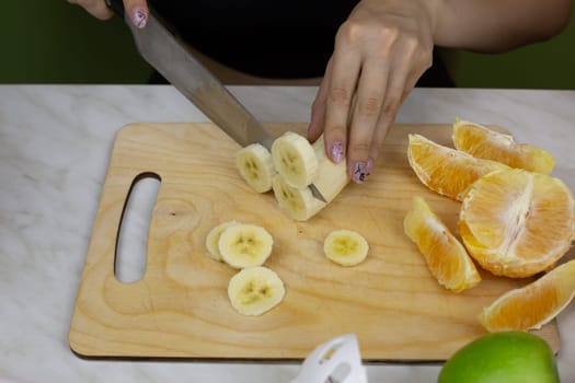 Girl cuts banana into pieces for easy blending while preparing sports drink from fruits. Healthy tonic smoothie for healthy lifestyle