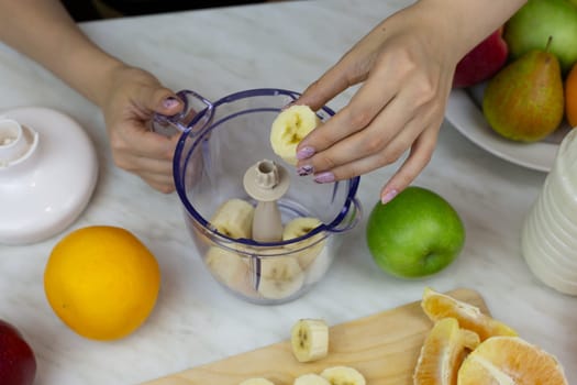 Women hands put banana pieces in container for grinding with blender, making tonic drink from fruits at home, simple recipe for healthy drink with vitamins