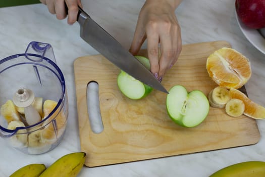 Women hands cutting an green apple into pieces for blender, chopping fruits to make sports cocktail with vitamins, healthy tonic drink at home