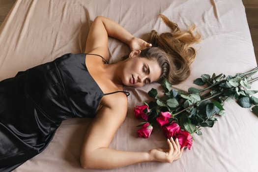 A woman is laying on a bed with a bouquet of red roses next to her. Concept of romance and intimacy, as the woman is surrounded by the flowers and he is in a relaxed and comfortable position