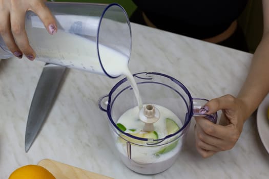 Women hands pour milk into blender according to recipe for milkshake with fruits. Healthy drink with vitamins at home according to simple recipe