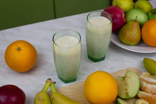 Two glasses with milkshake with vitamins on table with fruits. Ready made sports drink for improving health, refreshing drink with fruits and milk to boost vitamins
