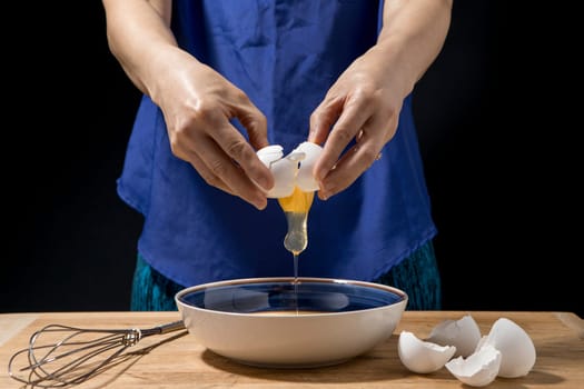A woman cracks open and egg and the yolk falls to the bowl.