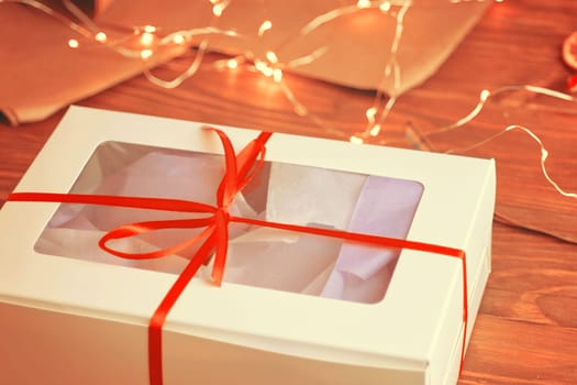 Christmas composition with present box. A Christmas gift box with a red ribbon stands on a wooden table.