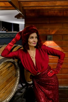 A woman in a red dress and red gloves poses in front of a barrel. Scene is elegant and sophisticated