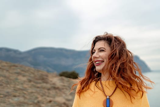 Portrait windswept hair happy woman against a backdrop of mountains and sea. Daylight illuminates the tranquil outdoor setting.