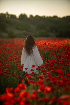 A woman in a white dress walks through a field of red poppies, the setting sun casting a warm glow on the scene.