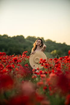 A woman in a white dress and straw hat stands in a field of red poppies, smiling and looking down at her hat. The setting sun casts a warm glow over the scene.