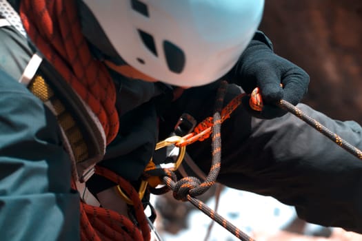 A hiker, a climber in a white helmet descends on a rope down the cliff, a close-up view of a hand in a fleece glove, with which a man holds on to a rock ledge.