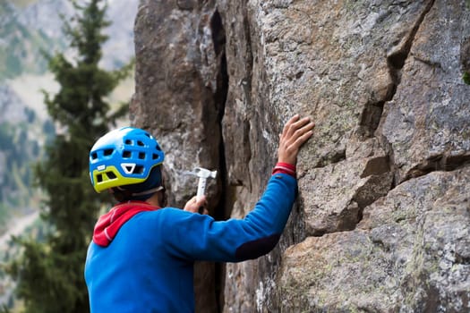 Young man checks the strength of the relief with a hammer, ..is engaged in extreme sports, an active lifestyle, climbs a mountain, a rock with equipment, wearing a helmet, with a rope and carabiners.