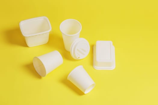 Disposable, white plastic cups with a lid, containers, boxes, on a yellow paper background.