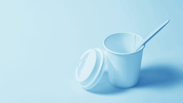 Disposable paper cup with a plastic lid and a plastic spoon on a blue paper background.