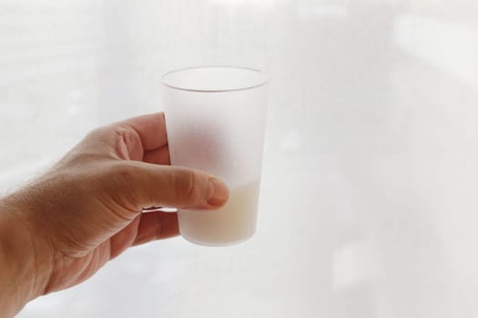 A man's hand close-up holds a transparent frosted glass with liquid.