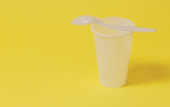A plastic glass with a spoon lying on it on a yellow paper background.
