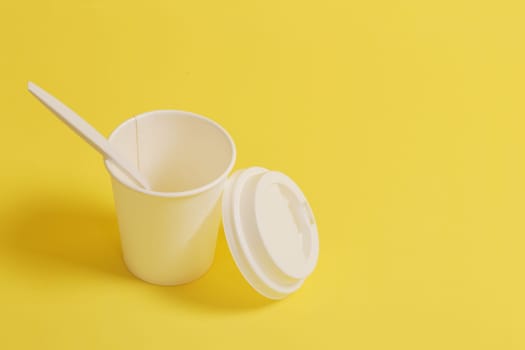 Disposable glass with a lid, with a teaspoon on a yellow background.