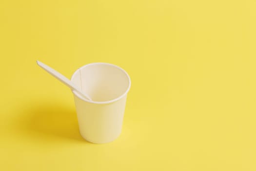 Disposable paper cup with spoon on a yellow background.