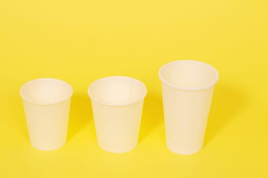 Three white plastic disposable cups on a yellow paper background.