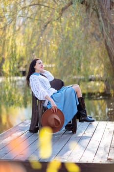 Autumn lake woman. She sits by a pond on a wooden pier in autumn and admires nature. The concept of tourism, weekends outside the city