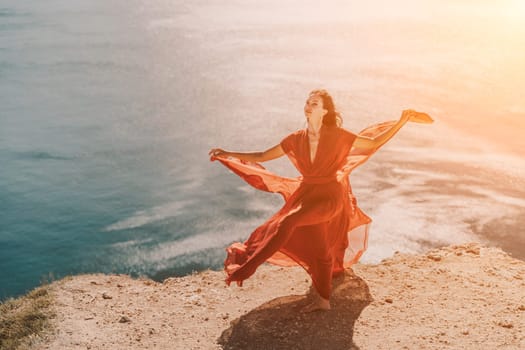Woman red dress sea. Female dancer in a long red dress posing on a beach with rocks on sunny day. Girl on the nature on blue sky background