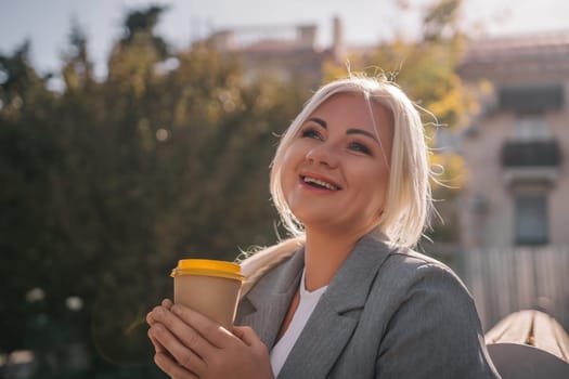 A blonde woman sits on a bench drinking coffee from a yellow cup. She is wearing a gray jacket and has her hair in a ponytail. The scene is peaceful and relaxing