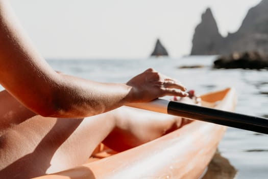 A person paddles a kayak in the ocean, their hand gripping the oar. The coastline is visible in the distance.