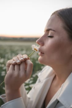 A woman is sitting in a field of flowers and is smelling a flower. The scene is peaceful and serene, with the woman enjoying the beauty of nature