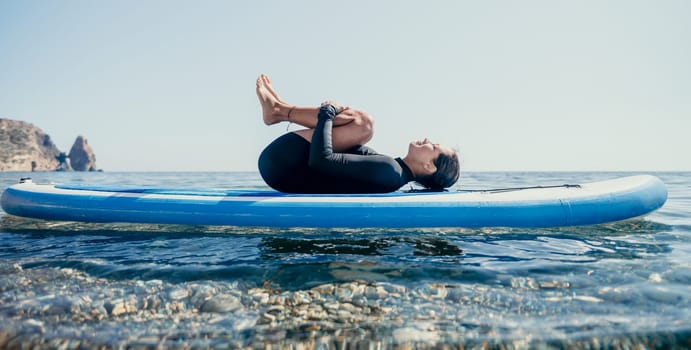 Woman sup yoga. Middle age sporty woman practising yoga pilates on paddle sup surfboard. Female stretching doing workout on sea water. Modern individual hipster outdoor summer sport activity