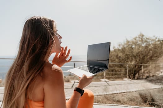 A young woman, sitting outdoors, looks surprised and holds a laptop open in front of her.