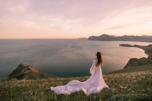 A woman in a white dress stands on a hill overlooking the ocean. The scene is serene and peaceful, with the woman's dress flowing in the wind. The ocean in the background is calm and inviting