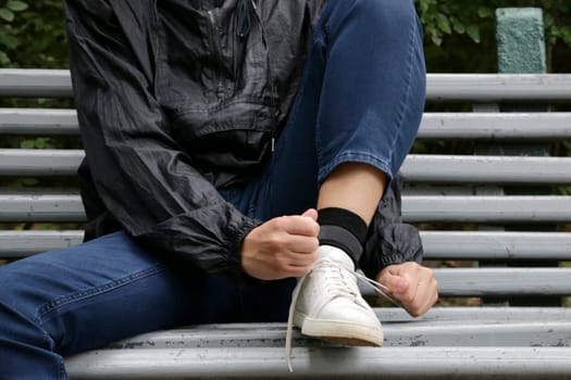 A boy in blue jeans and a blue windbreaker ties his laces on white sneakers.