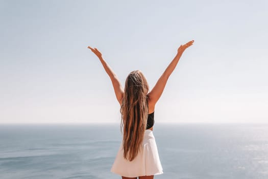 A woman with long hair stands on a beach, arms raised in the air, and the ocean is in the background
