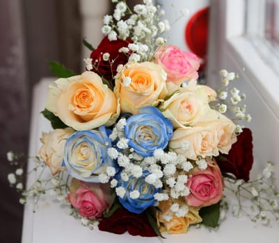 The bride's wedding bouquet with red, pink, blue flowers lies on the windowsill.
